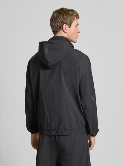Männermodel trägt Regular Fit Jacke mit Kapuze von adidas Sportswear in Schwarz, Elastischer-Material-Mix, Logo-Print, Ganzkörperansicht Rückansicht.