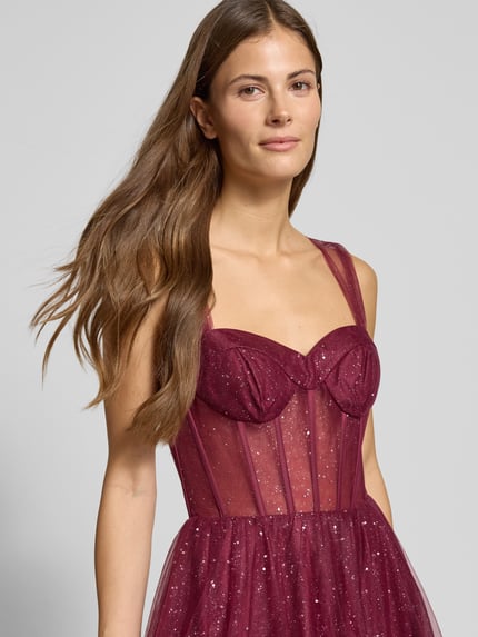 Modelka kobieca nosi Schimmerndes Abendkleid in semitransparenter Optik od Hey Kyla, bordowy tiul, błyszcząca tekstura, zbliżenie na górną część ciała.
