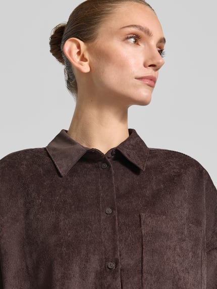Frauenmodel trägt Oversized Fit Langarmbluse mit Brusttasche Modell 'SANNE' von VERO MODA in Dunkelbraun, feine Cordstruktur, Nahaufnahme Oberkörper, Damen Langarmbluse von VERO MODA.