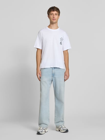 Männermodel trägt Relaxed Fit T-Shirt aus reiner Baumwolle Modell "DYLAN" von JACK & JONES, Print-Detail, weiße Farbe, Ganzkörperansicht von vorne.