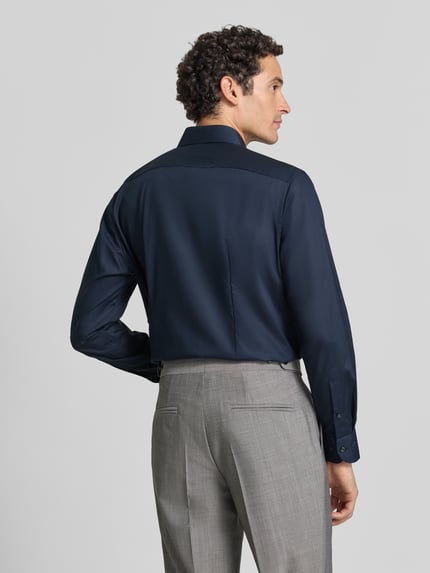 Männermodel trägt Regular Fit Businesshemd mit Kentkragen von OLYMP in Dunkelblau, feines Webstruktur, Ganzkörperansicht Rückansicht.
