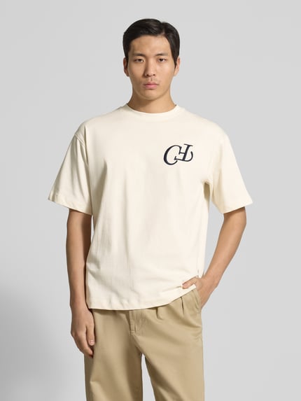 Männermodel trägt Herren T-Shirt aus reiner Baumwolle Modell 'KARLBERG' von Casual Friday, lockere Passform, Rundhalsausschnitt, Label-Stitching, Label-Print, helle Farbe, weiche Textur, Ganzkörperansicht von vorne.
