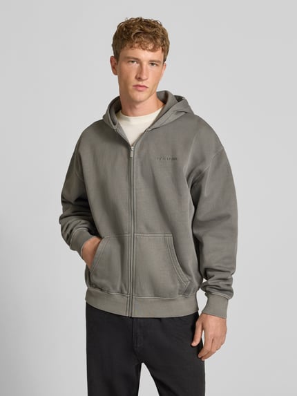 Männermodel trägt Regular Fit Sweatjacke aus Baumwoll-Mix von PEGADOR in Grau mit Logo-Stickerei, Kängurutasche, Zipper, Ganzkörperansicht von vorne.
