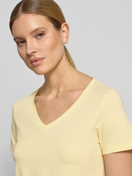 Kobiece model nosi damski t-shirt Regular Fit T-Shirt aus Baumwoll-Mix od s.Oliver RED LABEL, efekt: jednolity kolor, dekolt w serek, krótki rękaw, wykończenie materiału: dżersej, mieszanka bawełny, jasny żółty kolor, gładka faktura, zbliżenie górnej części ciała, przód.