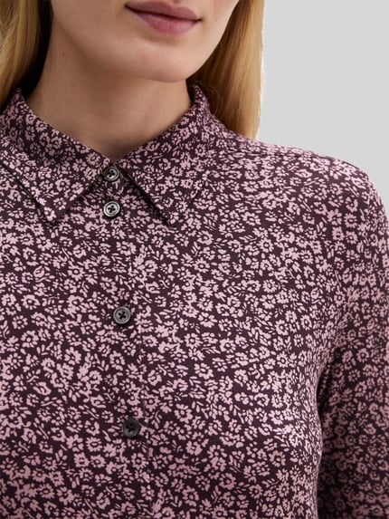 Frauenmodel trägt Longline Langarmbluse mit Label-Detail von Marc O'Polo, abstraktes Allover-Muster in Lila und Rosa, Nahaufnahme Oberkörper.