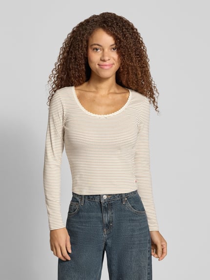 Frauenmodel trägt Slim Fit Langarmshirt aus Baumwoll-Mix von Levi's® 300, beige mit feinen Streifen, strukturierte Textur, Ganzkörperansicht von vorne.