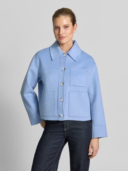 Modelka kobieca nosi Jacke mit aufgesetzten Taschen Modell 'Helia' od OPUS w kolorze jasnoniebieskim, bawełniany miks z domieszką wiskozy, krój relaxed fit, kołnierz wykładany, zapięcie na guziki, naszywane kieszenie, długość pleców w rozmiarze S: 55 cm, szerokość ramion w rozmiarze S: 48 cm, szerokość w biuście w rozmiarze S: 56 cm, długość rękawa w rozmiarze S: 56 cm, gładka faktura, widok całej sylwetki z przodu