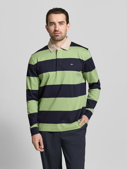 Männermodel trägt Regular Fit Poloshirt mit Streifenmuster und Label-Stitching von Fynch-Hatton, Farbkontraste grün und navy, reine Baumwolle, Knopfverschluss, Polokragen, Longsleeve, Ganzkörperansicht von vorne.