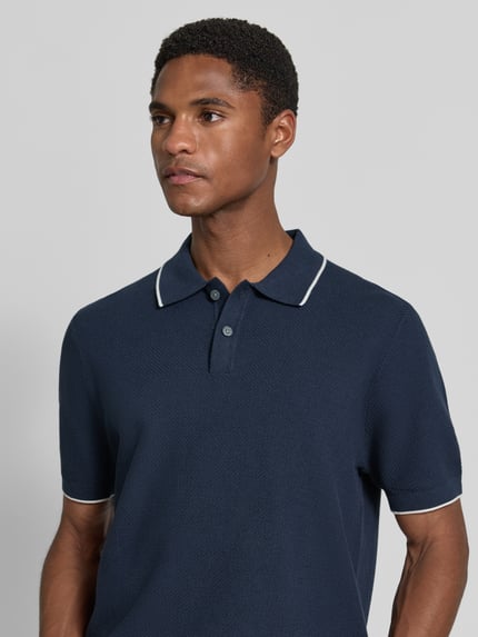 Męski model ma na sobie Regular Fit Poloshirt mit Kontrastkante von Christian Berg Men, granatowa bawełna, struktura, kołnierzyk polo, krótka lista guzikowa, kontrastowe krawędzie, długość tyłu 67 cm, długość rękawa 30 cm, ujęcie z przodu, zbliżenie na górę ciała.