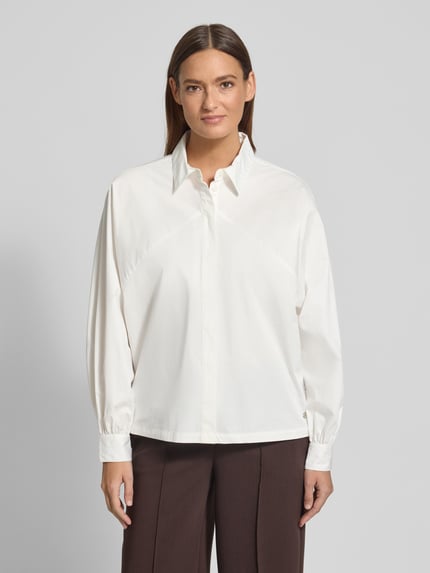 Frauenmodel trägt Regular Fit Hemdbluse mit Hemdblusenkragen von Fynch-Hatton, Reine Baumwolle, Logo-Applikation, Langärmelig, Sportmanschetten, Rückenlänge 64 cm, Ärmellänge 56 cm, weiß, Ganzkörperansicht von vorne.
