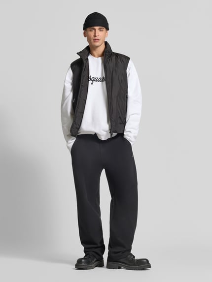 Männermodel trägt schwarze Weste mit Zweiwege-Reißverschluss von Dsquared2, gerader Schnitt, Stehkragen, Reißverschlusstaschen, Ganzkörperansicht von vorne