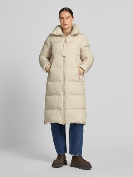 Frauenmodel trägt Regular Fit Daunenmantel mit abnehmbaren Rucksackriemen von Marc O'Polo in Beige, glatte Struktur, Ganzkörperansicht von vorne. Damen Daunenmantel von Marc O'Polo