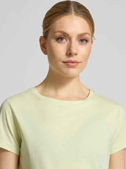 Vrouwenmodel draagt Slim Fit T-Shirt uit zuivere katoen model 'ELOVE_EMBRO' van BOSS Orange, effen geel met logo-stiksel, ronde hals, korte mouw, close-up bovenlichaam
