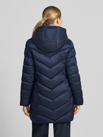 Frauenmodel trägt Steppmantel mit Kapuze und Reißverschlusstaschen von MICHAEL Michael Kors in Dunkelblau, glatte Struktur, Ganzkörperansicht Rückansicht. Gerader Schnitt, Rückenlänge 86 cm, Schulterbreite 43 cm, Brustweite 50 cm, Ärmellänge 62 cm, Kapuze mit Tunnelzug und Kordelstopper, Stehkragen, seitliche Reißverschlusstaschen.