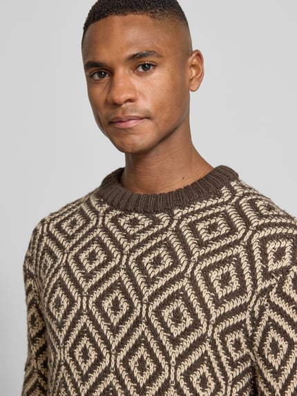 Männermodel trägt Relaxed Fit Strickpullover aus Woll-Mix Modell 'REMI' von SELECTED HOMME mit Allover-Muster in Braun und Beige, Nahaufnahme Oberkörper.