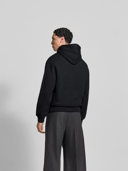 Mężczyzna nosi Hoodie mit Label-Stitching od MAISON KITSUNÉ w czerni, luźny krój, kaptur, długość tyłu 65 cm, całkowity widok z tyłu.