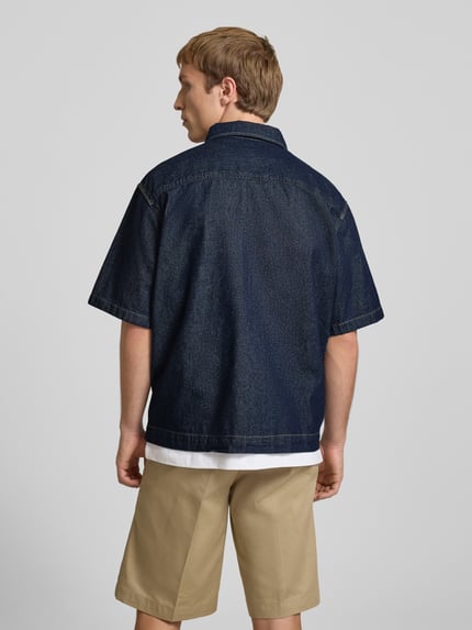 Männermodel trägt Relaxed Fit Jeanshemd mit Brusttasche von Dickies aus Reine Baumwolle in dunklem Blau, Rückenlänge 69 cm, Ganzkörperansicht Rückansicht.