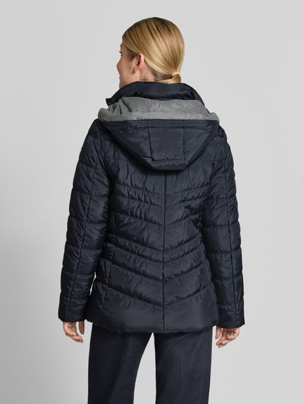 Männermodel trägt kurtka 'Jacke in Stepp-Optik mit Kapuze' od FUCHS SCHMITT, kolor granatowy, z efektem pikowania, krój taliowany, kaptur, stójka z ociepleniem, wpuszczane kieszenie z zamkiem błyskawicznym, długość tyłu w rozmiarze 36: 74 cm, szerokość ramion w rozmiarze 36: 40 cm, szerokość w klatce piersiowej w rozmiarze 36: 48 cm, długość rękawów w rozmiarze 36: 64 cm, całkowity widok z tyłu