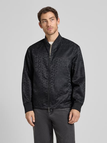 Männermodel trägt Blouson mit Zweiwege-Reißverschluss von ARMANI EXCHANGE in Schwarz, Gerader-Schnitt, Stehkragen, Ganzkörperansicht von vorne, Rückenlänge 67 cm, Schulterbreite 51 cm, Brustweite 61 cm, Ärmellänge 66 cm, gerippte Ärmelabschlüsse, dezentes Logo-Muster.