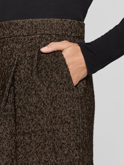 Frauenmodel trägt Weite Hose mit Woll-Anteil Modell 'Tianara' von BOSS, braunes Fischgrät-Muster, grobe Textur, Nahaufnahme Oberkörper, Damen Weite Hose von BOSS.