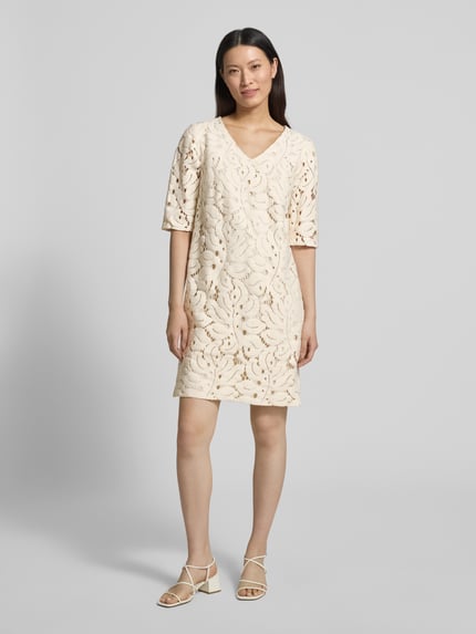 Modelka nosi 'Knielanges Kleid mit Lochstickerei' od Betty Barclay, mieszanka bawełny i wiskozy, prosty krój, długość do kolan, haft angielski, dekolt w serek, odcień kremowy, długość tyłu 92 cm, szerokość w rozmiarze 36: 48 cm, długość rękawów 34 cm, widok całej sylwetki z przodu.