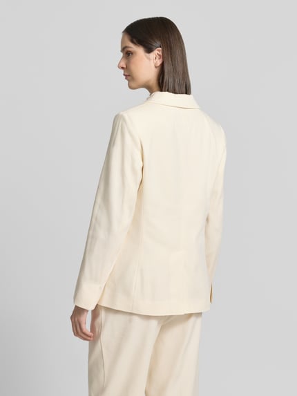 Frauenmodel trägt Blazer mit Pattentaschen Modell 'Nulani' von Someday in hellem Beige, glatte Textur, Rückenansicht, Ganzkörperansicht. Material-Mix mit Baumwoll-Anteil, Straight Fit, Reverskragen, Knopfverschluss, Rückenlänge 68 cm, Brustweite 44 cm, Ärmellänge 62 cm.