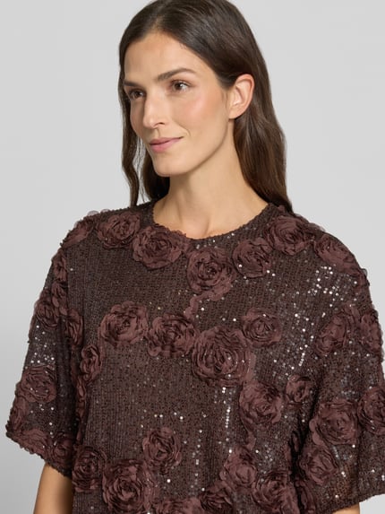 Frauenmodel trägt Blusenshirt mit Pailletten Modell 'ELYSIA' von YAS, brauner Material-Mix, florale 3D-Textur, Nahaufnahme Oberkörper.