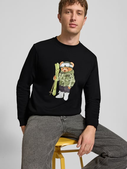 Męski model nosi Sweatshirt mit Motiv-Print od CHILL PILL, mieszanka bawełny, krój regular fit, okrągły dekolt, czarny, nadruk z motywem misia, Długość tyłu w rozmiarze M: 68 cm, Długość rękawów w rozmiarze M: 66 cm, pełny widok z przodu.