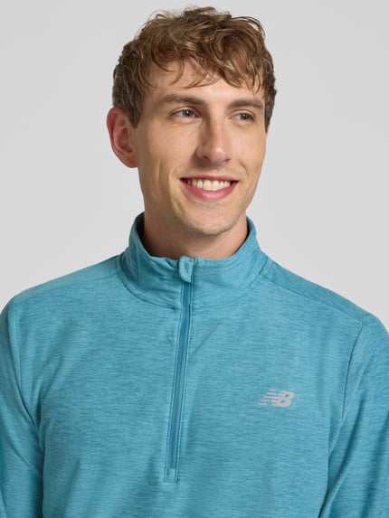 Męski model nosi Regular Fit Sweatshirt mit Troyer-Kragen od New Balance, elastyczna mieszanka materiałów, krój regular fit, nadruk z logo, długość tyłu w rozmiarze M: 69 cm, zbliżenie na górną część tułowia