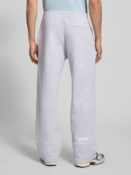 Mannenmodel draagt sweatpants met elastische band en logo van REVIEW in lichtgrijs, puur katoen, relaxed fit, binnenbeenlengte maat M 78 cm, geheellichaamsaanzicht achteraan.