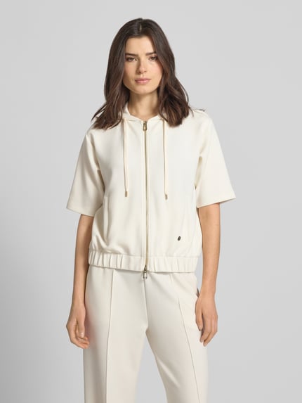 Frauenmodel trägt Sweatjacke mit Halbarm Modell 'Therese' von JOOP! in Creme, Elastischer-Material-Mix, Gerader-Schnitt, Kapuze mit Tunnelzug, Reißverschluss, Halbarm, Label-Detail, Elastischer-Bund, Eingrifftaschen, glatte Textur, Ganzkörperansicht von vorne.