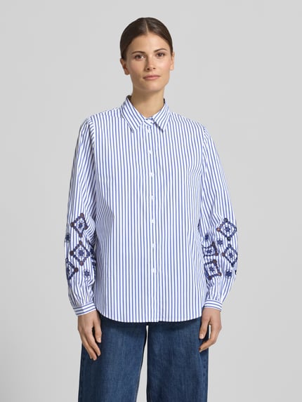 Kobiece model nosi Regular Fit Bluse mit Lochstickerei od Apricot, mieszanka bawełny z dodatkiem streczu, krój regular fit, haft angielski na rękawach, kołnierzyk koszulowy, listwa guzikowa, długość tyłu w rozmiarze S: 69 cm, długość rękawów w rozmiarze S: 61 cm, białe i niebieskie pionowe paski, guziki białe, całkowity widok z przodu.