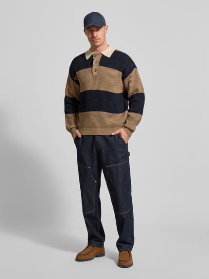 Männermodel trägt Poloshirt mit gerippten Abschlüssen Modell 'Lotu' von WOODBIRD im lockeren Schnitt, beige-blau gestreift, Ganzkörperansicht von vorne.