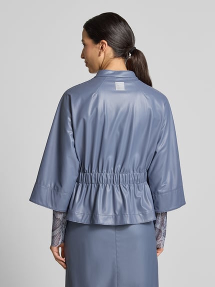 Frauenmodel trägt Blazer in Leder-Optik mit Stehkragen von Marc Cain, taillierte Passform, 3/4-Arm, glänzende Oberfläche, Ganzkörperansicht Rückansicht.
