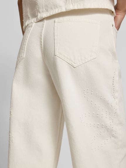 Frauenmodel trägt Wide Fit Jeans in verkürzter Passform Modell 'Dexter' von MSCH Copenhagen, bawełna, 5 kieszeni, kremowy kolor, widoczne szwy i faktura materiału, Knopf- und zamek błyskawiczny, Szerokość w rozmiarze S: 38 cm, długość wewnętrzna nogawki w rozmiarze S: 74 cm, Ganzkörperansicht Rückansicht.