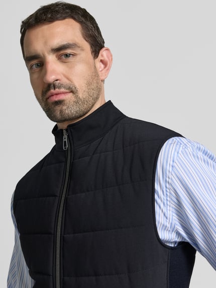 Männermodel trägt Steppweste mit Eingrifftaschen Modell 'Wento' von JOOP!, Slim Fit, schwarz, geradlinige Steppung, Nahaufnahme Oberkörper.