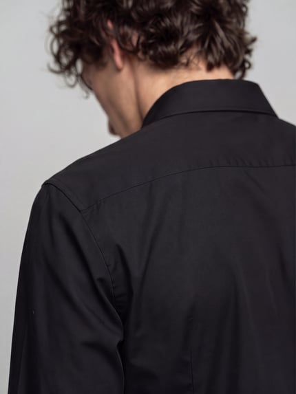 Männermodel trägt Body Fit Businesshemd aus reiner Baumwolle von OLYMP Level 5 in Schwarz, glatte Textur, Ganzkörperansicht Rückansicht.