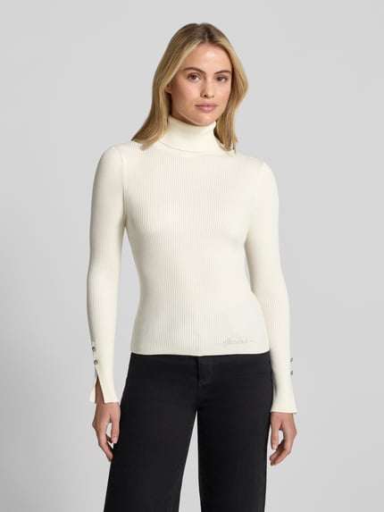 Kobiece modelka nosi Strickpullover aus Viskose-Mix mit Rollkragen od GUESS, krój slim fit, Efekt prążkowania, Detal z logo, długość tyłu 54 cm, długość rękawów 62 cm, kolor ecru, widok całej sylwetki z przodu.