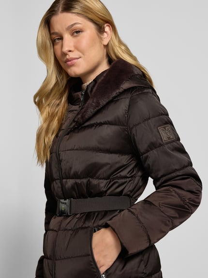 Kobiece modelka ma na sobie Steppjacke mit Reißverschlusstaschen und Gürtel od monari, ciemnobrązowy kolor, krój slim fit, kaptur ze sztucznym futerkiem, dwukierunkowy zamek błyskawiczny, kieszenie z zamkami, pasek, długość pleców w rozmiarze 36: 67 cm, szerokość ramion w rozmiarze 36: 42 cm, szerokość w rozmiarze 36: 49 cm, długość rękawa w rozmiarze 36: 62 cm, zbliżenie na górną część ciała z przodu