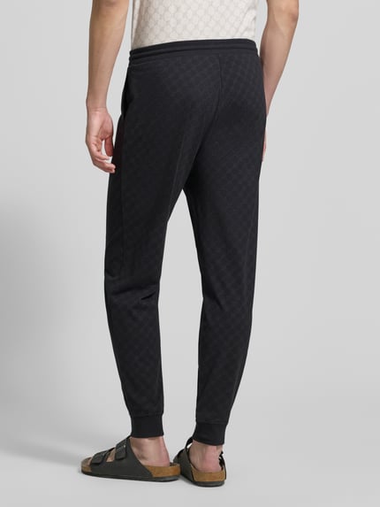 Męski model nosi Sweatpants mit Logo-Muster und elastischem Bund od JOOP! Collection, czarny kolor, krój regular fit, logo, bawełna, widok całej sylwetki z tyłu.
