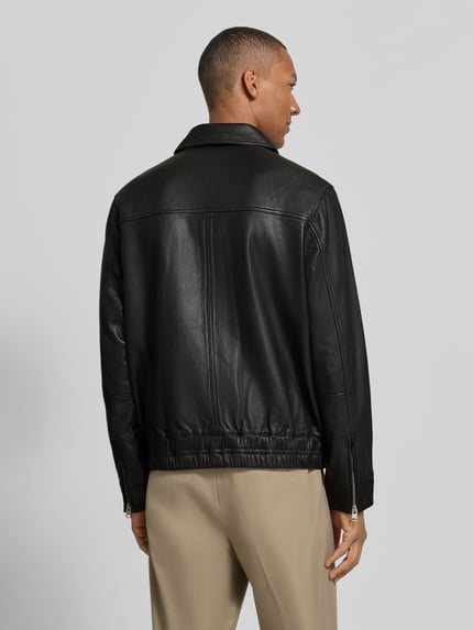 Męski model nosi Regular Fit Lederjacke aus Schafsleder von AllSaints, czarna skóra owcza, krój regular fit, Model 'arto', kołnierzyk typu kent, zamek błyskawiczny dwustronny, kieszeń na piersi zapinana na zamek, boczne kieszenie wsuwane i z patką, widok całej sylwetki z tyłu.