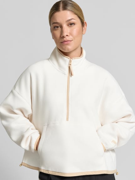 Frauenmodel trägt Relaxed Fit Pullover Troyer-Kragen Modell 'Polar' von Fabletics, Damen Fleecejacke in Creme mit Kängurutasche, Nahaufnahme Oberkörper.