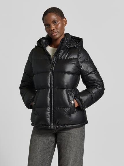 Frauenmodel trägt Regular Fit Steppjacke mit Logo-Emblem von MICHAEL Michael Kors in Schwarz, gesteppte Optik, Kapuze, Eingrifftaschen, glänzende Textur, elastische Ärmelabschlüsse, durchgehender Zipper, Ganzkörperansicht von vorne.