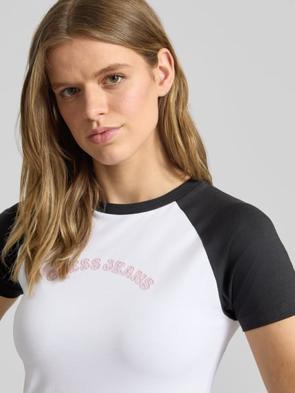 Vrouwenmodel draagt Slim Fit T-shirt met ronde hals en logo van Guess Jeans in mix van katoen en elastaan, wit en zwart, logoprint, ruglengte bij maat S 53 cm, nahaufnahme bovenlichaam.