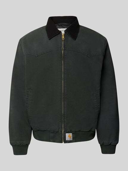 Produktfoto, Jacke mit Reißverschluss und Label-Detail Modell 'Santa Fe' von Carhartt Work In Progress aus reiner Baumwolle in Dunkelgrün, sichtbare Struktur, goldfarbener Reißverschluss, Umlegekragen, Regular Fit, neutrale graue Hintergrundfarbe.