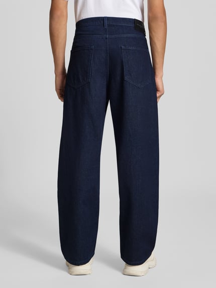 Männermodel trägt Wide Fit Jeans aus reiner Baumwolle von MAISON KITSUNÉ in Dunkelblau, 5-Pocket-Design, gleichmäßige Waschung, Ganzkörperansicht Rückansicht.