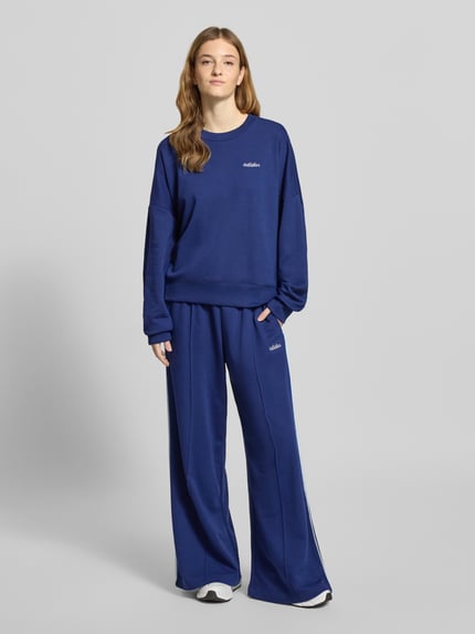 Frauenmodel trägt Sweatshirt mit Label-Stitching von adidas Sportswear in Blau, weiter Schnitt, Rundhalsausschnitt, Baumwoll-Mix, Ganzkörperansicht von vorne.