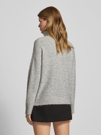 Frauenmodel trägt Oversized Rollkragenpullover mit Paillettenbesatz Modell 'ARIZONA LS SEQUINS' von Only in Hellgrau, Stricktextur, Effektgarn, gerippte Abschlüsse, Ganzkörperansicht Rückansicht.