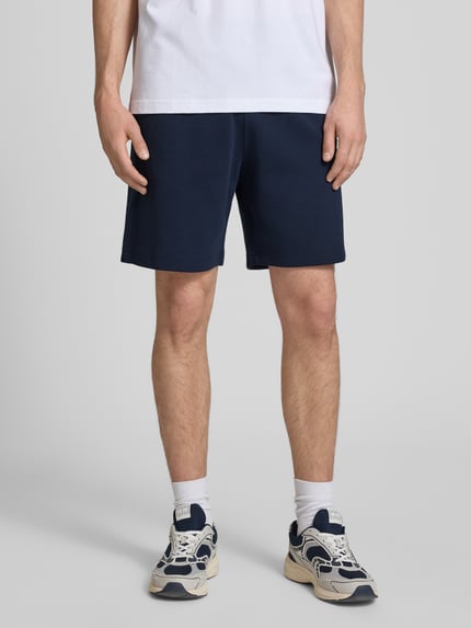 Männermodel trägt Shorts mit Label-Stitching mit elastischem Bund von CHAMPION in Dunkelblau, Baumwoll-Mix, Regular Fit, Ganzkörperansicht von vorne.