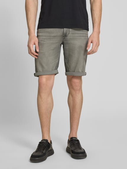Mężczyzna nosi Bermudas im 5-Pocket-Design mit aufgeschlagenem Saum od Christian Berg Men, bawełniany mix z domieszką stretchu, krój straight fit, pięć kieszeni, zapięcie na guzik i zamek, detal z logo, mankiet, szerokość w rozmiarze 32: 41 cm, długość nogawki od wewnątrz w rozmiarze 32: 26 cm, szare odcienie, gładka tekstura, widok całej sylwetki z przodu.